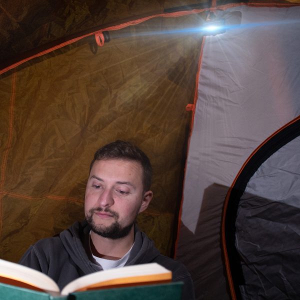 Camper using bright light from high quality Carson LED Keychain Flashlight with Hook for hands free use while camping to read in low light